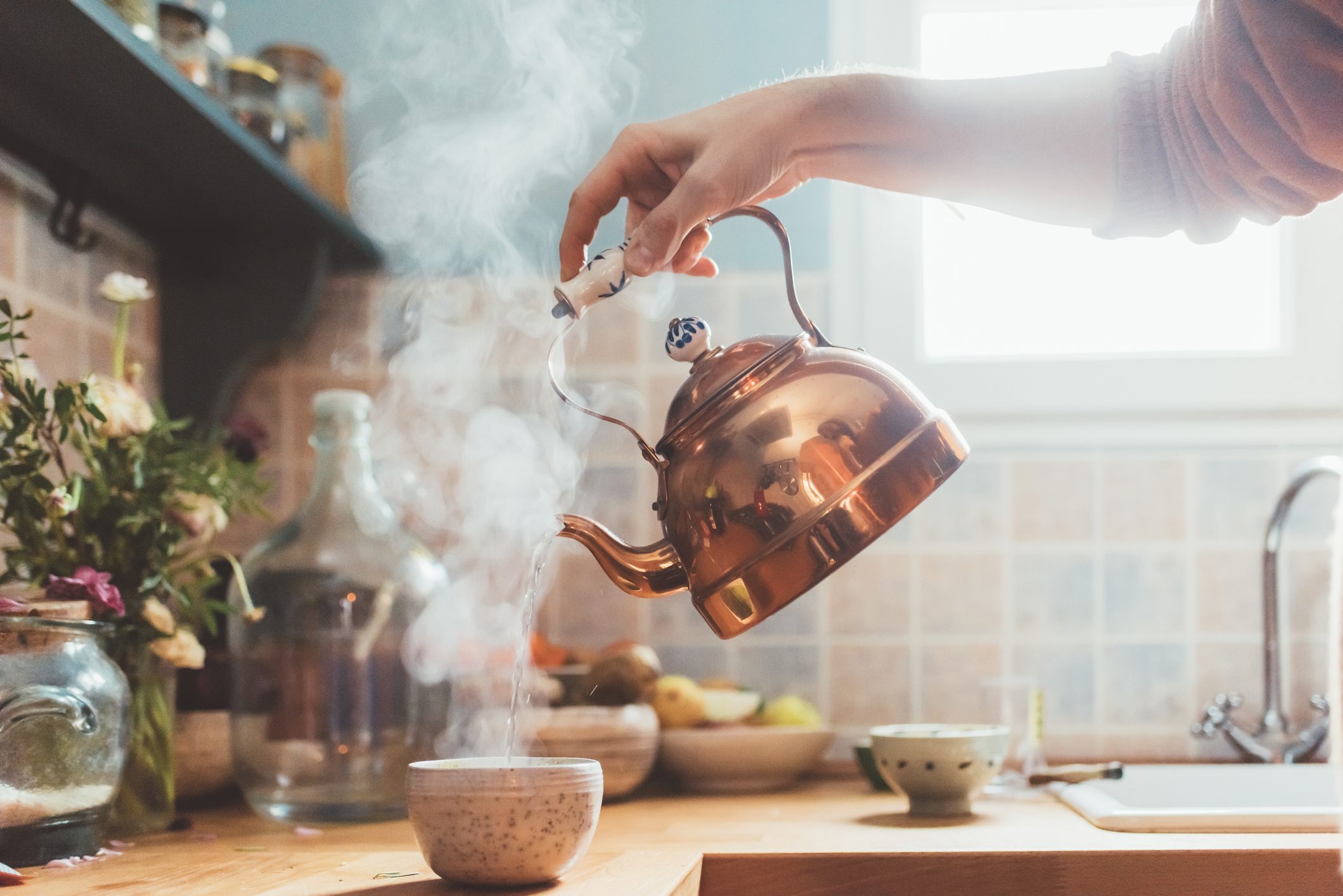 Arm of man pouring boiling water into bowl in kitchen