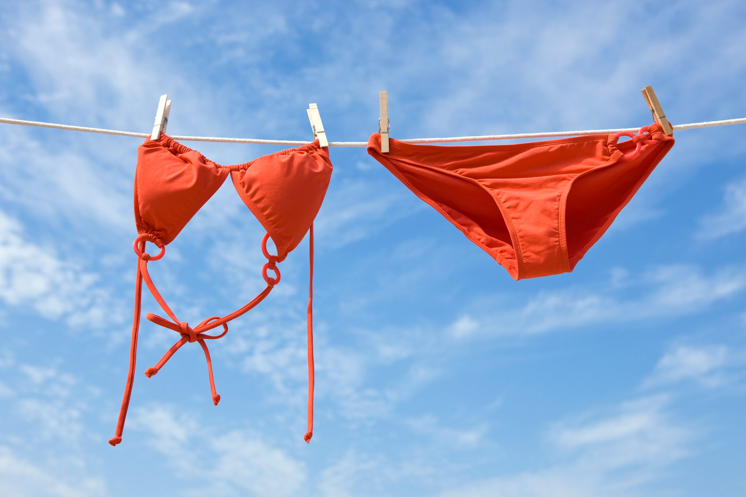 red bikini bathing suit hanging on a clothes line with blue sky in the background