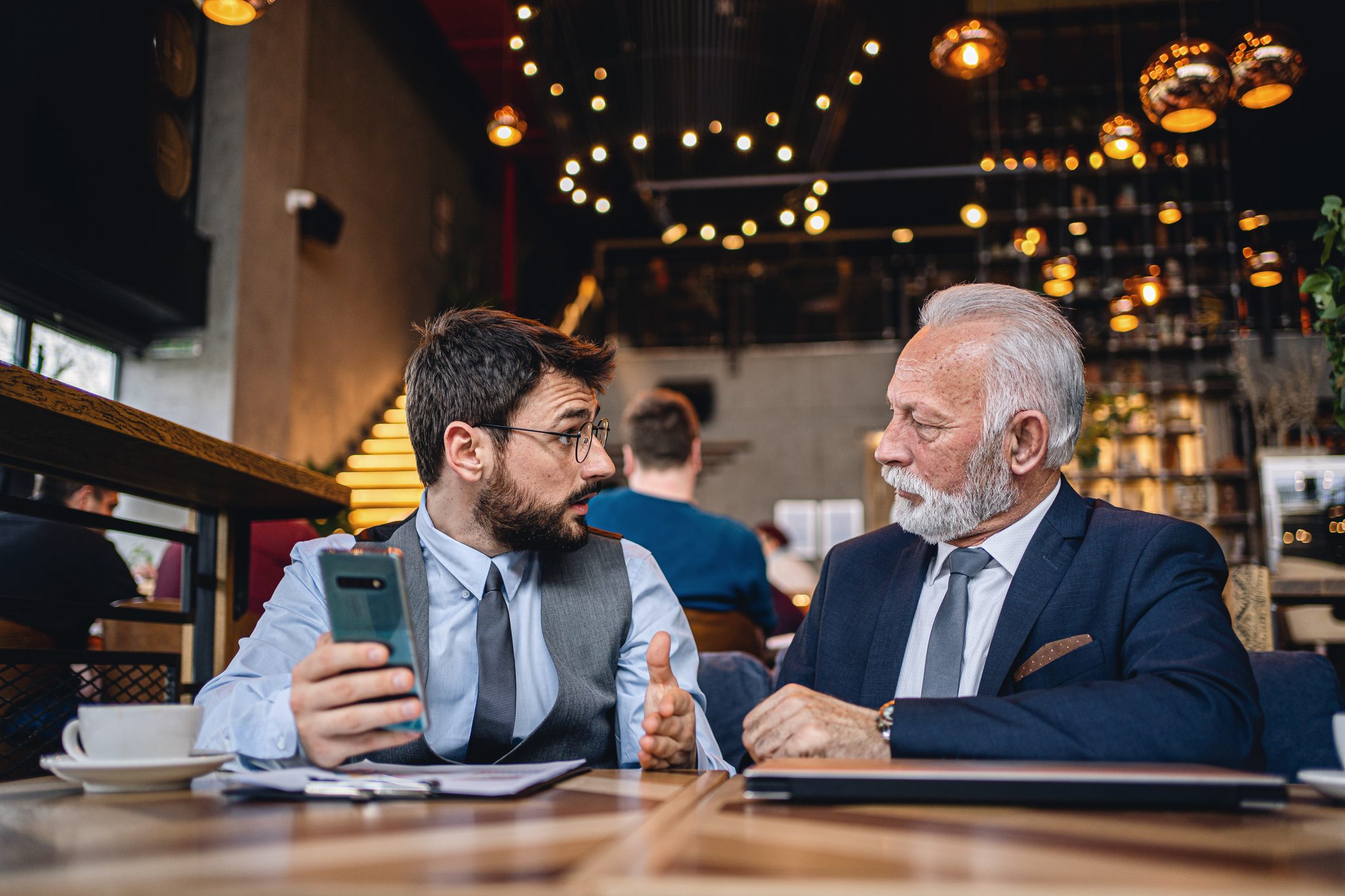 Senior businessman listening to a younger colleague's business strategy at a cafe