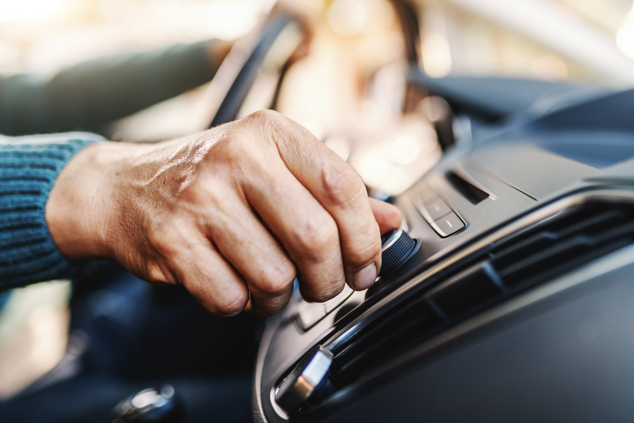 Close up of senior man changing radio station while sitting in his car.