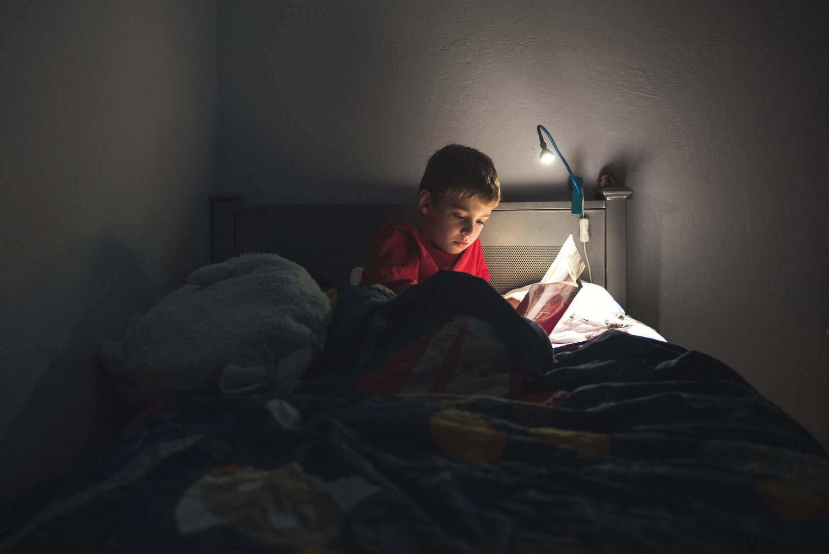 Boy reading in bed with reading lamp
