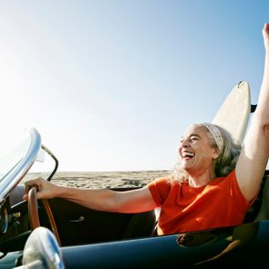 Older Caucasian woman in convertible car with surfboard on beach