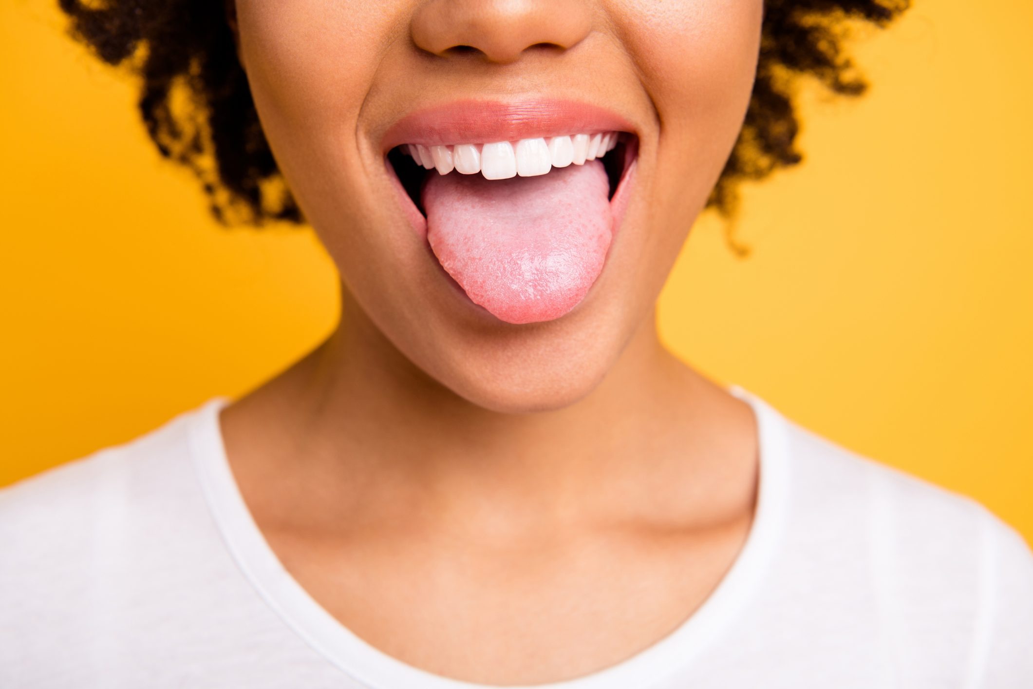 Cropped close up photo beautiful amazing she her dark skin lady beaming whitening toothy smile tongue out perfect mouth wear casual white t-shirt isolated yellow bright vibrant background