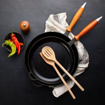 overhead view of two stacked cast iron skillet pans with crossed kitchen utensils