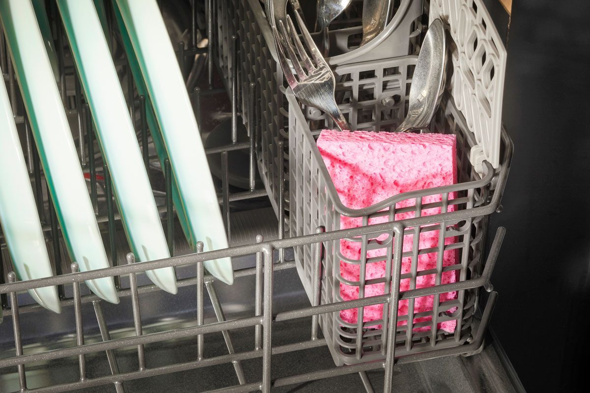 pink kitchen sponge in the silverware holder in a dishwasher