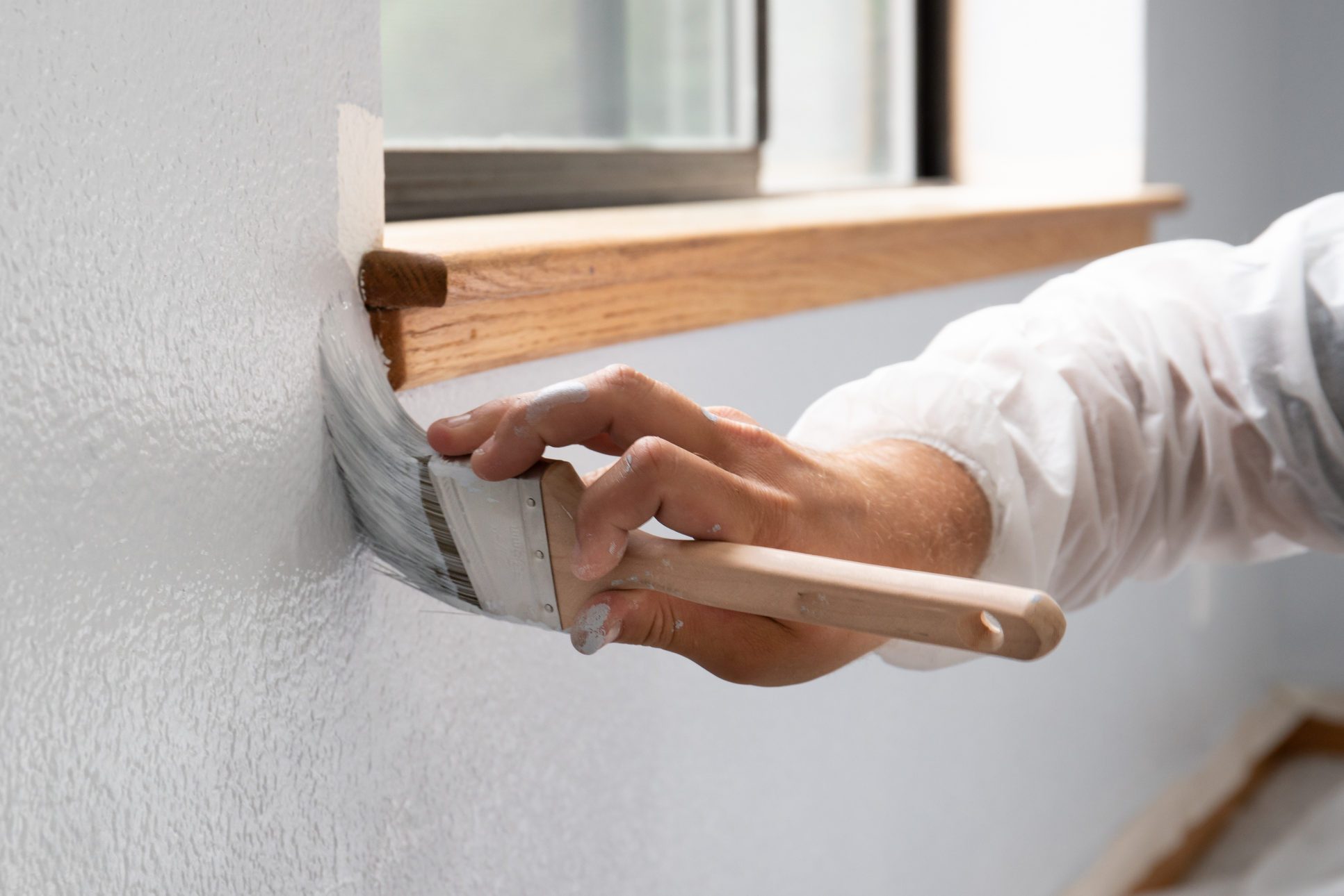 Man painting interior of home by window