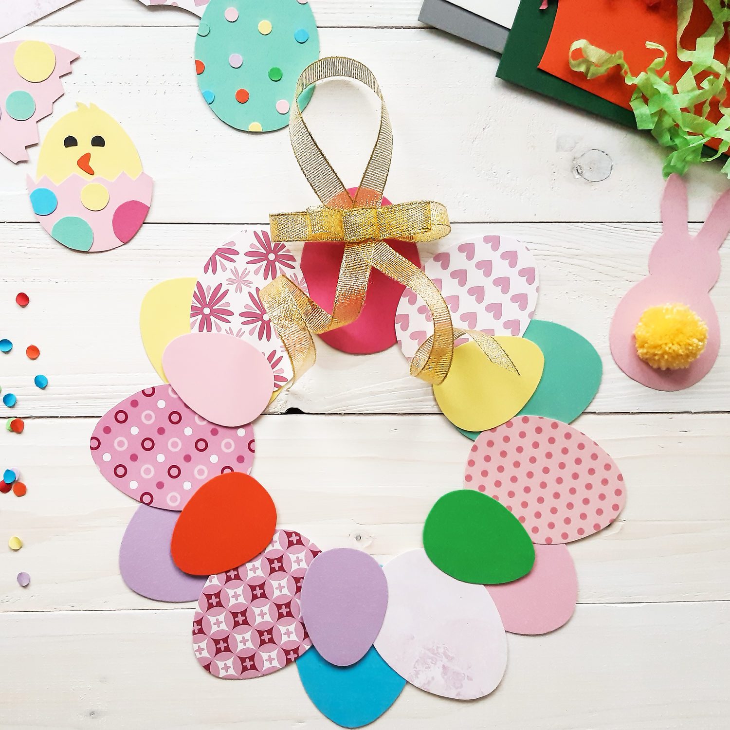 The child makes crafts with his own hands for the Easter. Colorful handmade from multi-colored paper. Scissors, cardboard, eggs, chicken, rabbit. Art creativity on a wooden table. Top view, copy space