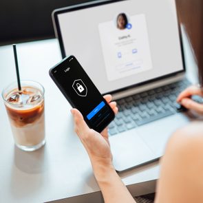 Young Business Woman Logging In Online Security System On Laptop With Mobile App On Smartphone