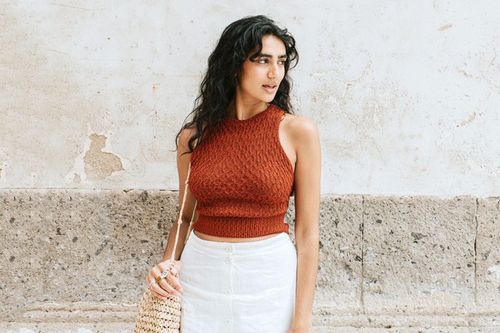 A stylish, elegant young woman with a small bag, stands outside, gazing off to the side