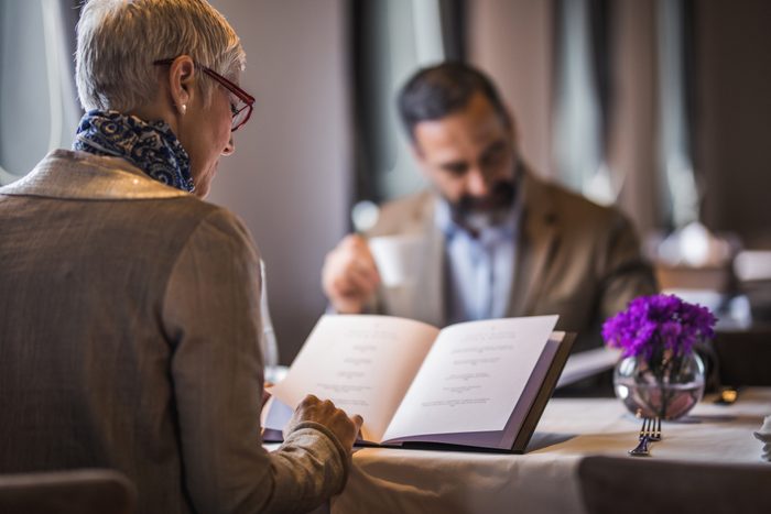Back view of mature woman reading Menu during lunch time in a restaurant.