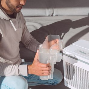 Man changing water container in air dryer, dehumidifier, humidity indicator. Humid air at home.