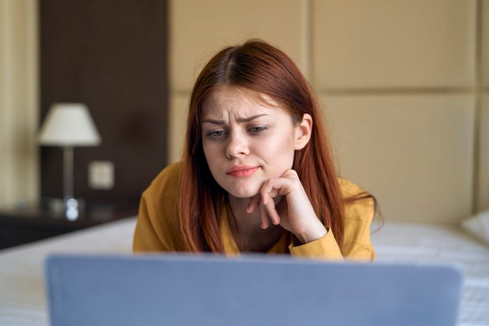 Confused Caucasian woman laying on bed using laptop