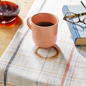 cup of coffee and a ring stain on fabric runner on a kitchen table. carafe and book nearby on the table