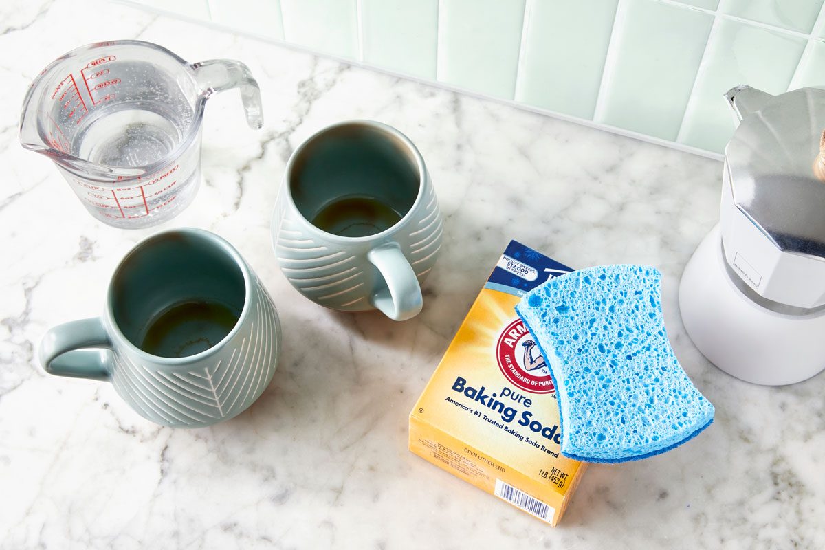 two mugs with coffee stains on a kitchen counter with supplies needed to clean them nearby