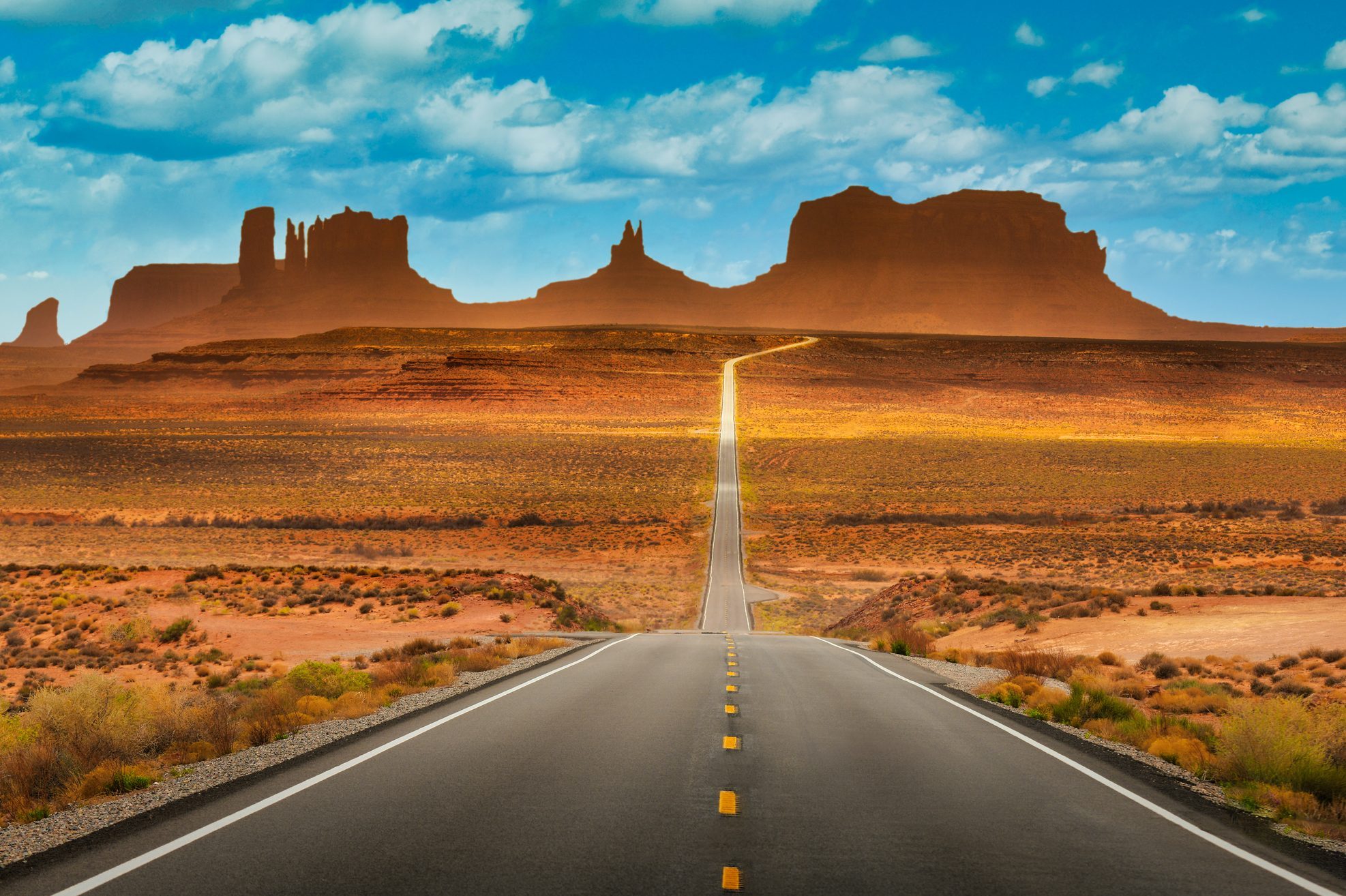 View of historic U.S. Route 163 running through famous Monument Valley in beautiful golden evening light at sunset on a beautiful sunny day with blue sky in summer, Utah, USA