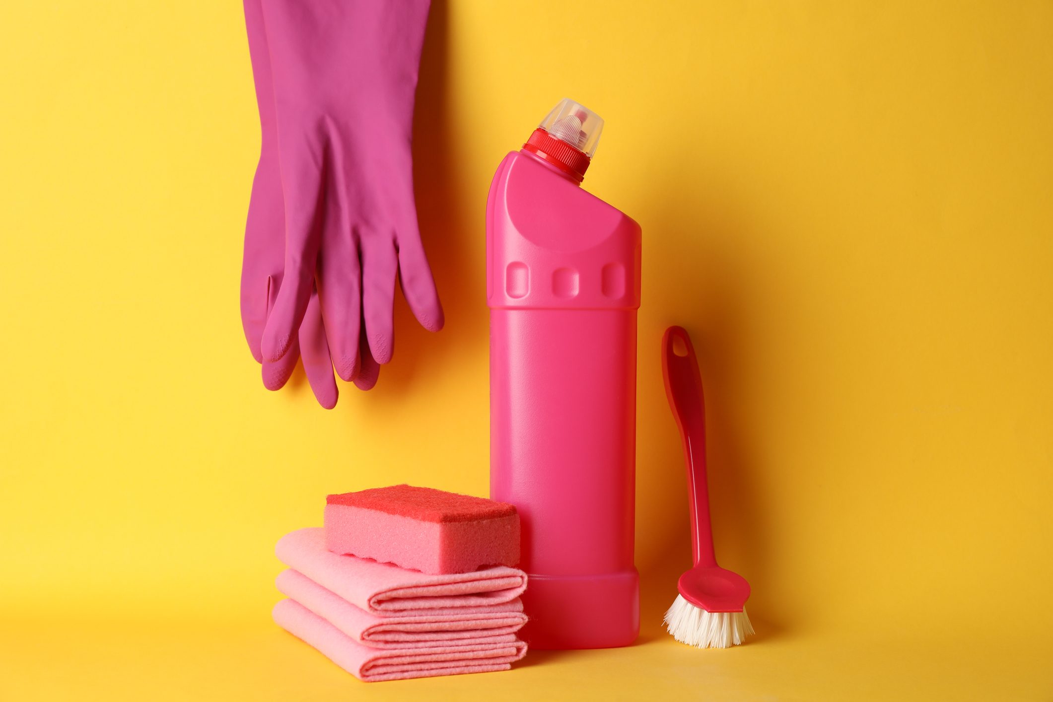 Bottle with detergent and cleaning supplies on yellow background, space for text