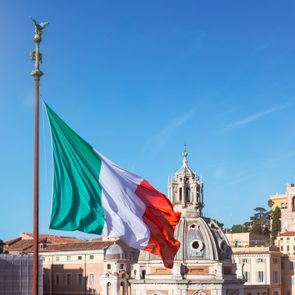 Italy, Rome, Italian flag fluttering against clear blue sky and dome of Santa Maria di Loreto