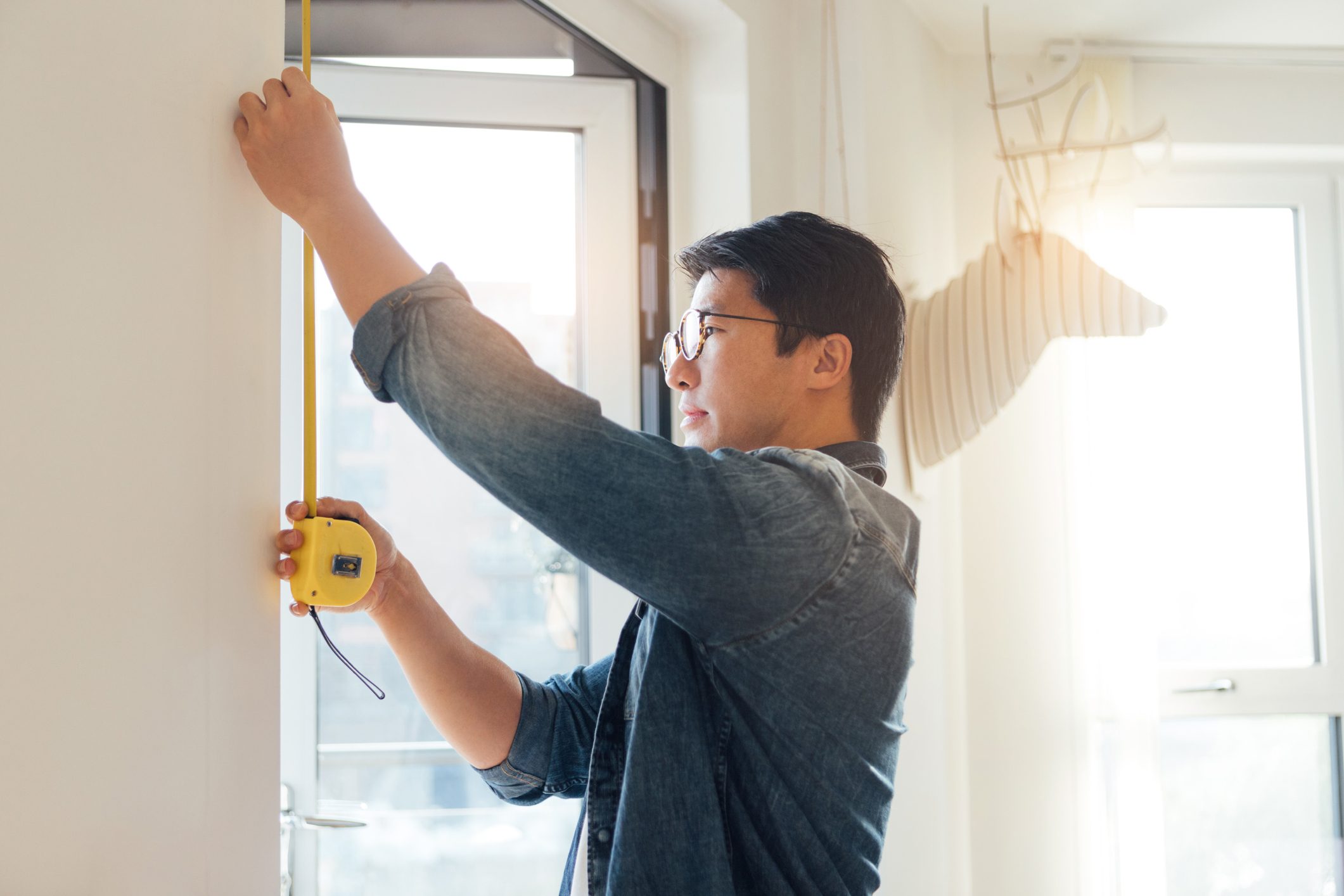 Focused young man doing DIY project at home using measuring tape.