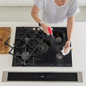 woman degreasing a black gas stovetop, viewed from overhead