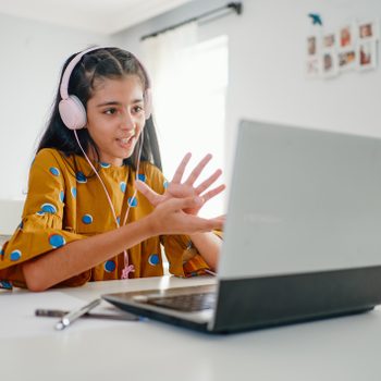 Teenage girl with headphones and laptop learning with online school class at home