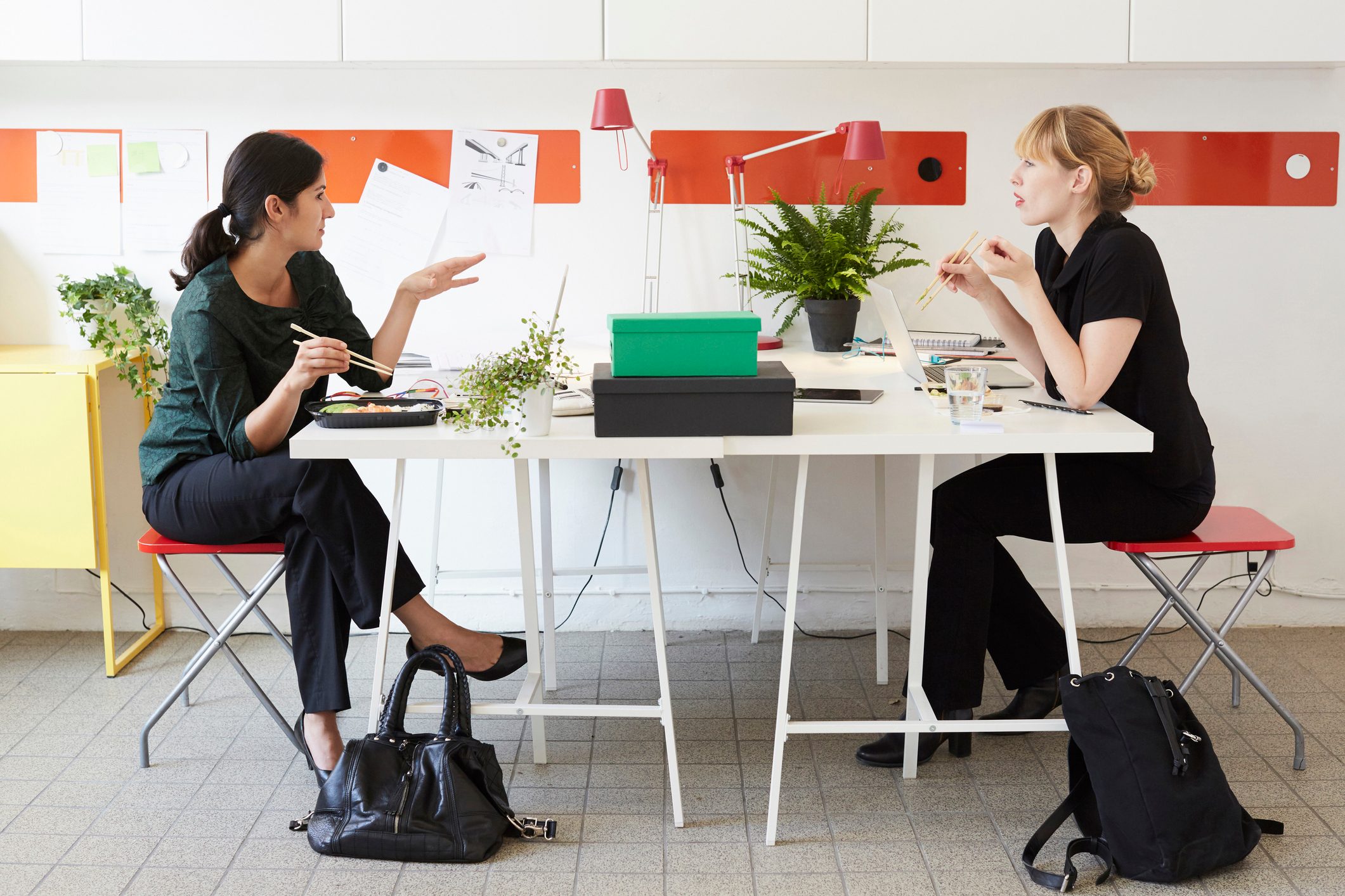 Full length of businesswomen talking while having lunch at table in office