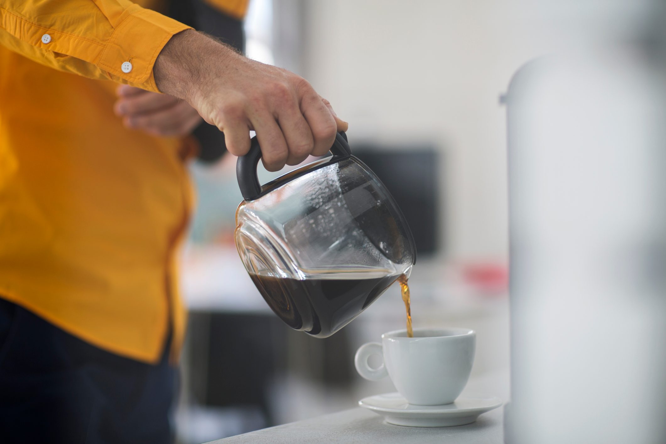 Employee with sling pouring coffee into cup at work