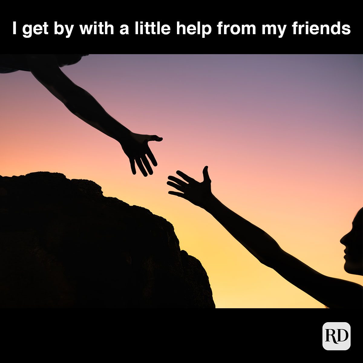 silhouette of person helping another get up a rock during sunset