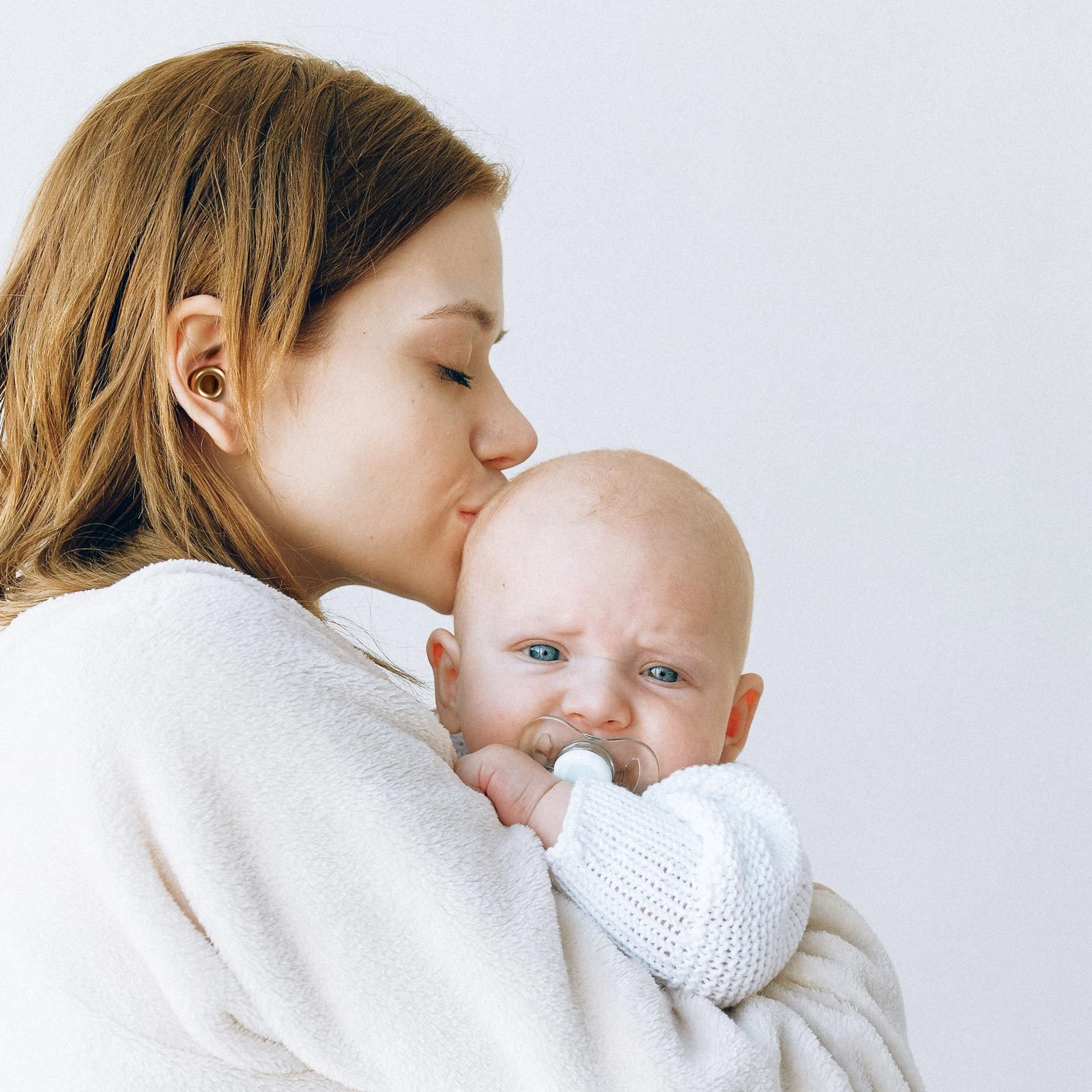 mother wearing loop earplugs kissing her baby