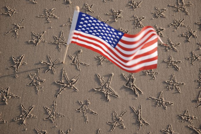an American flag waves above a stretch of sand with hand-drawn stars