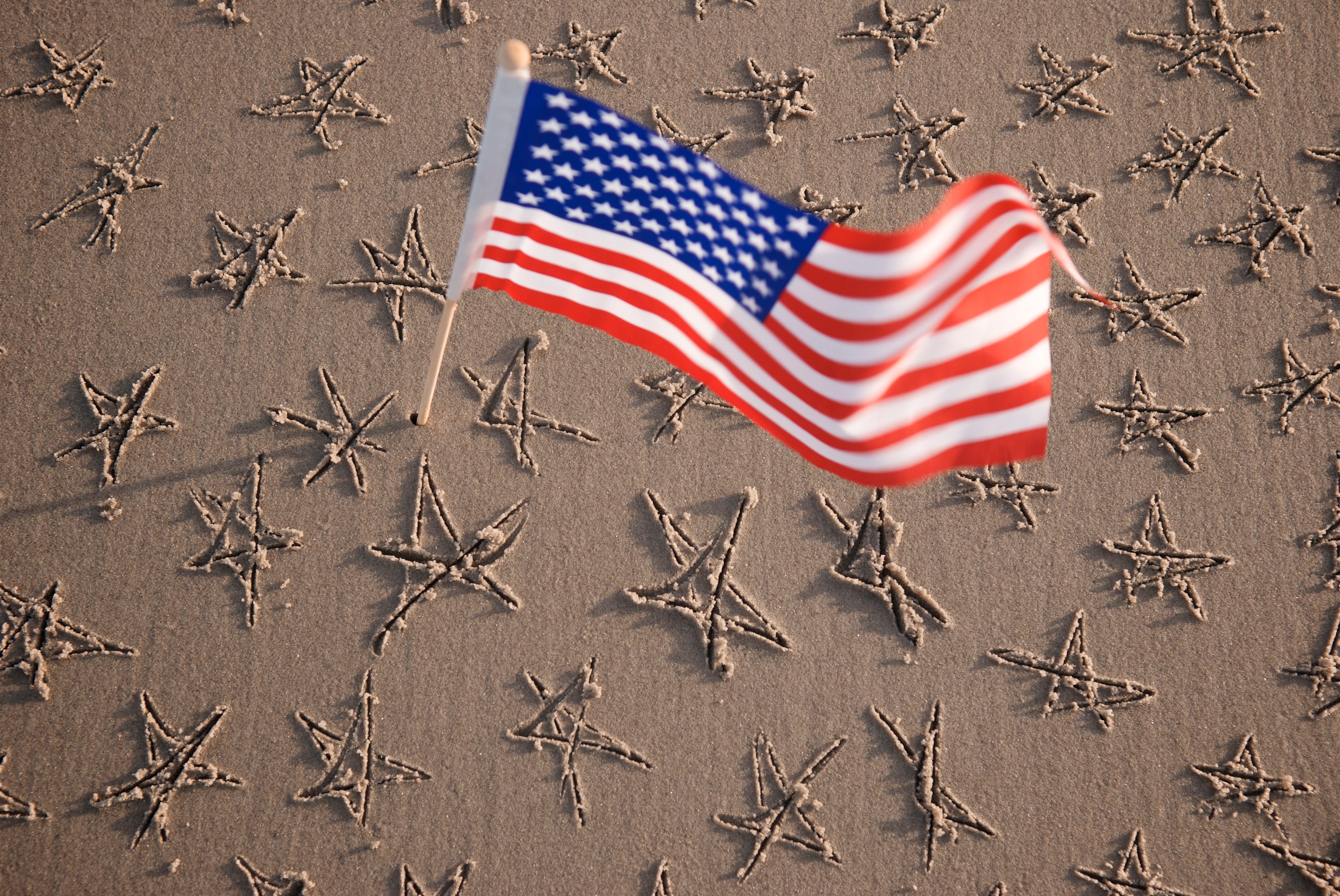 an American flag waves above a stretch of sand with hand-drawn stars