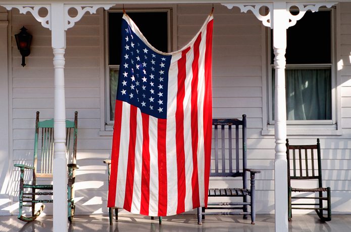 a larg american flag hanging on porch in front of four rocking chairs