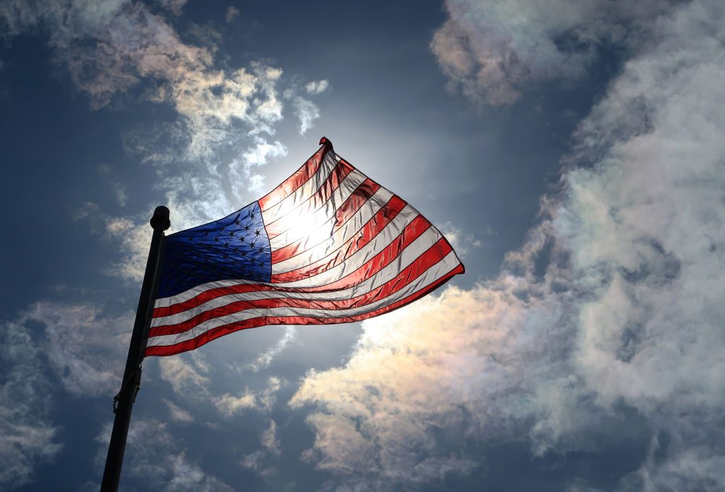 an upward view of the sun streaming through a wavy american flag against they sky in atlantic highlands, new jersey