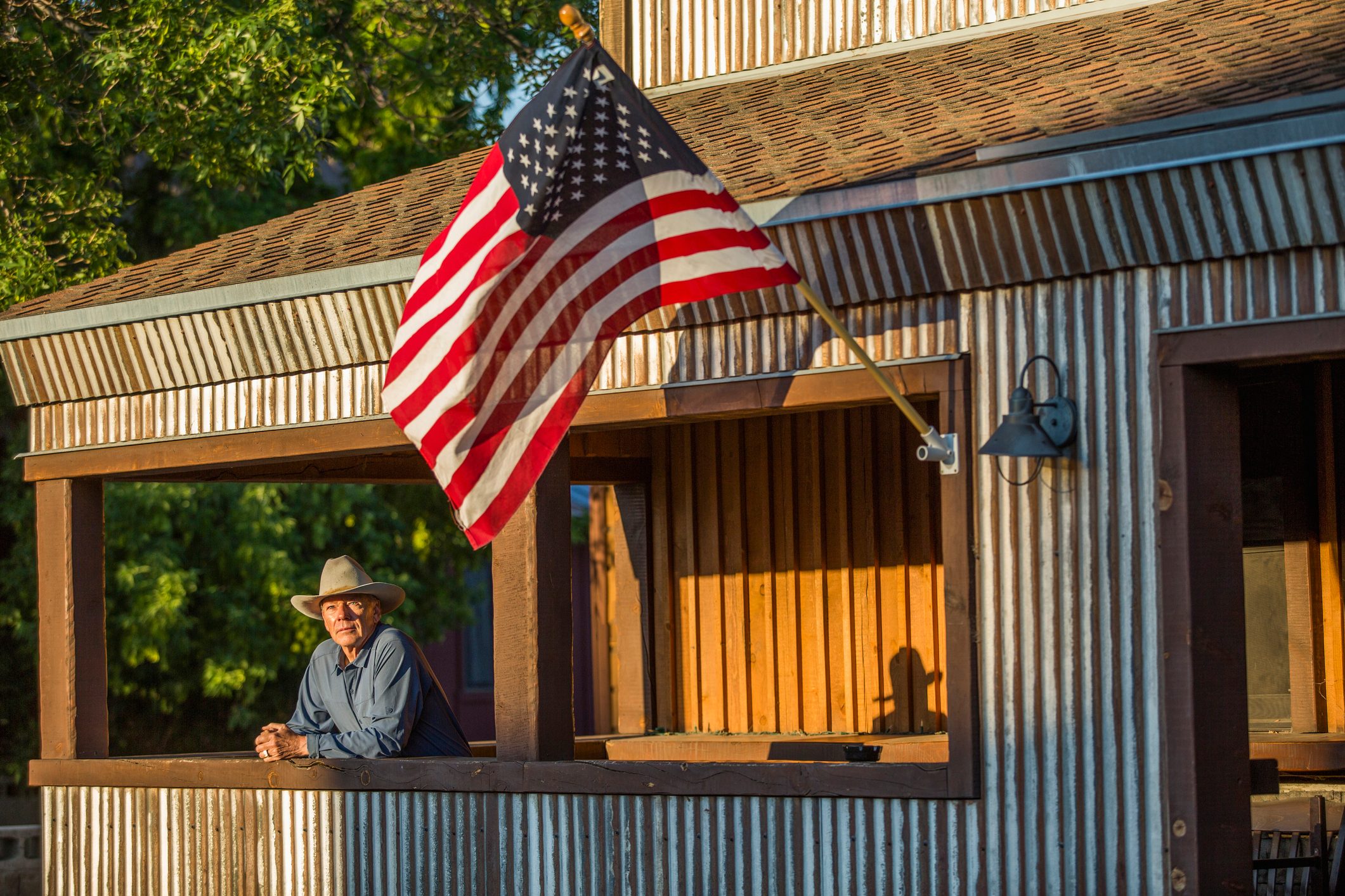 Serious farmer on his porch with an American flag in low, golden sunlight