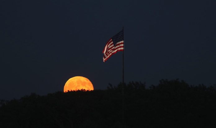 The moon rises behind a flag on Liberty Island in New York City on July 9, 2017 as seen from Jersey City, New Jersey.