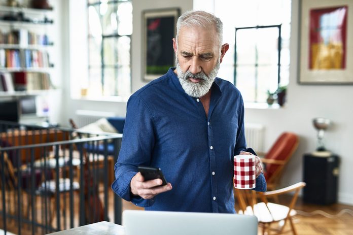 Senior creative professional remote working and checking phone at home