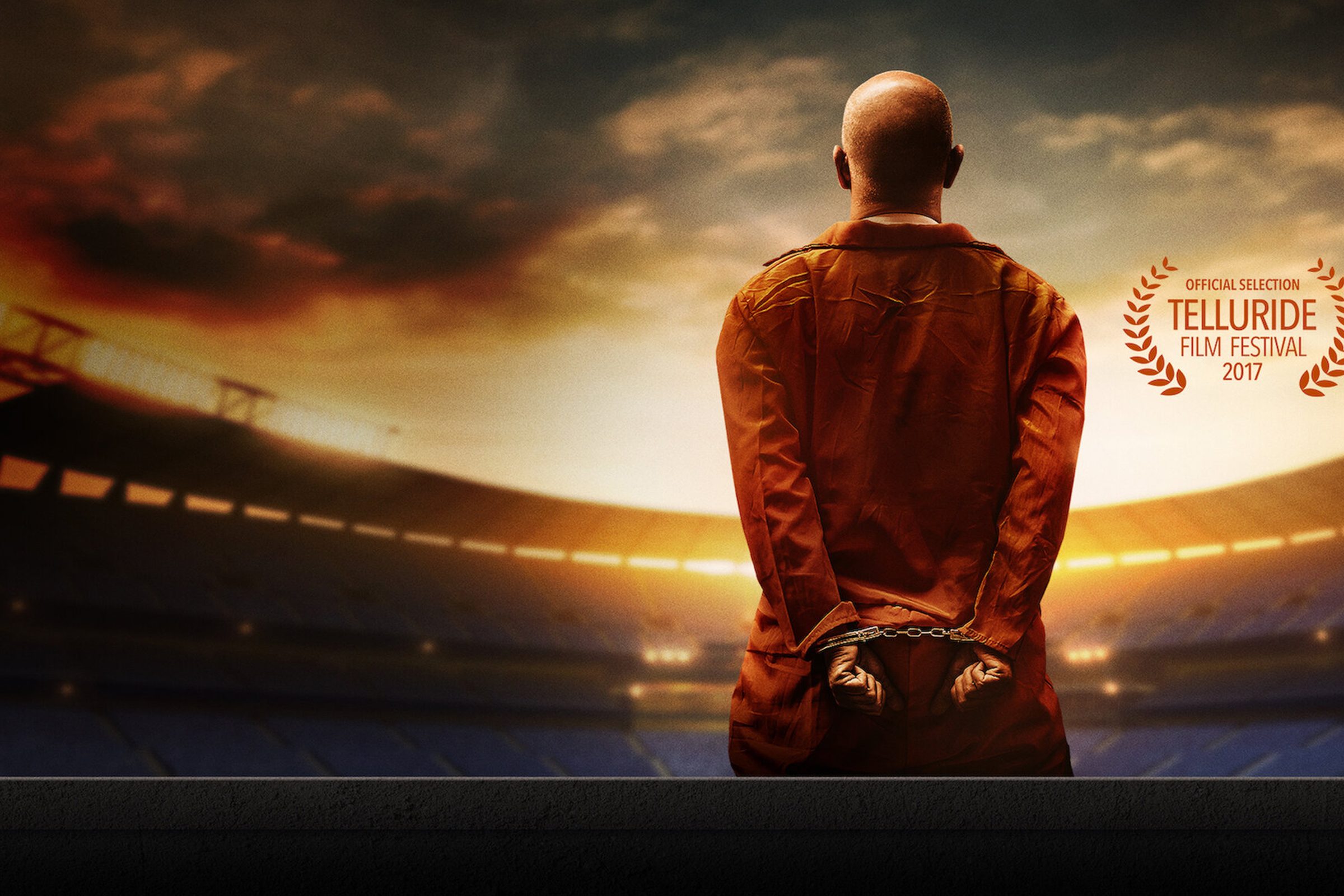 Man in jumpsuit and handcuffs standing in front of stadium