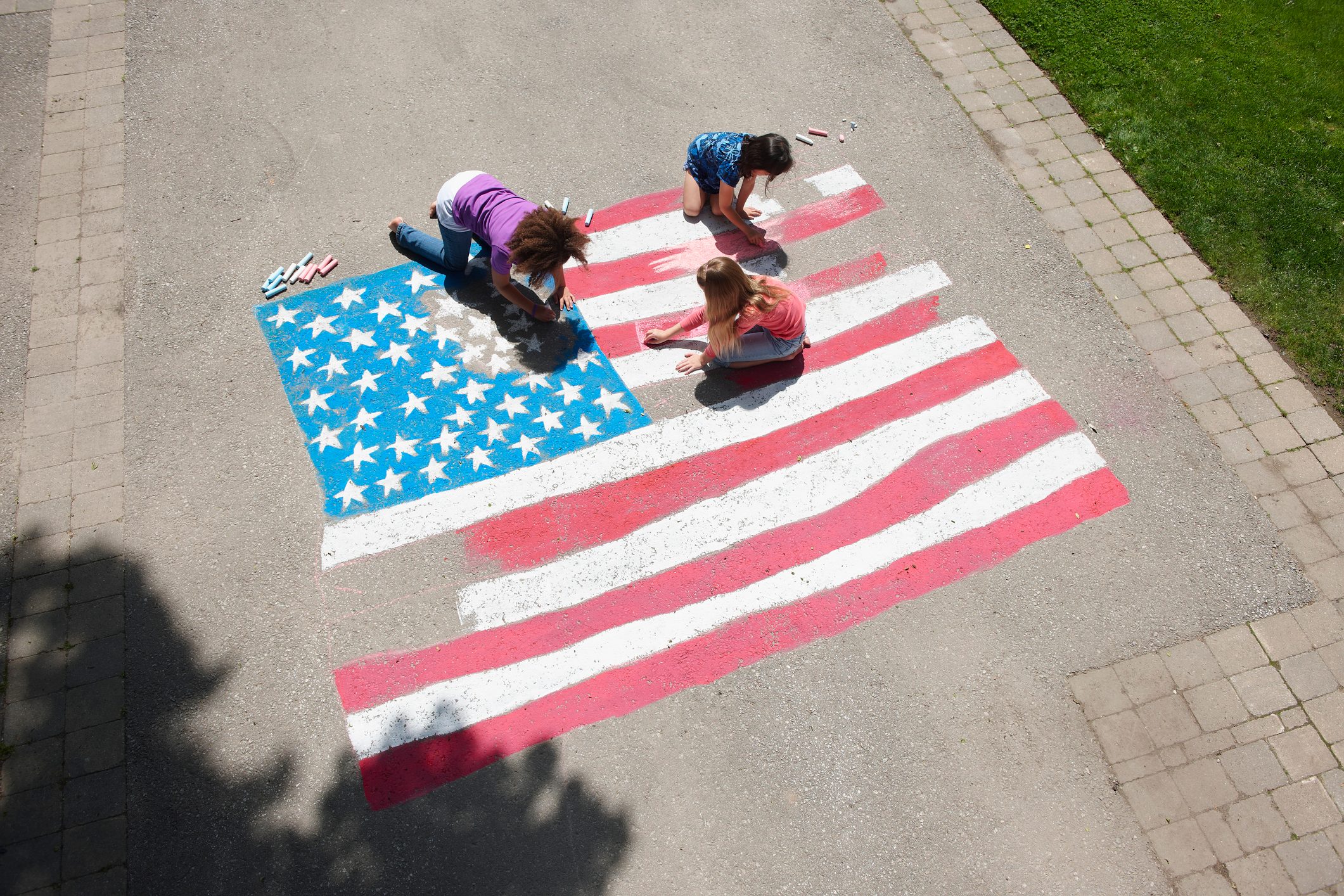 Girls with chalk coloring American flag on sidewalk