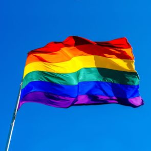 Rainbow flag waving in the wind against clear blue sky