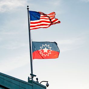 the american flag and the juneteenth flag wave atop a building with the early evening sky background
