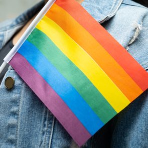 anonymous lgbtq ally wearing denim jacket and holding rainbow pride flag