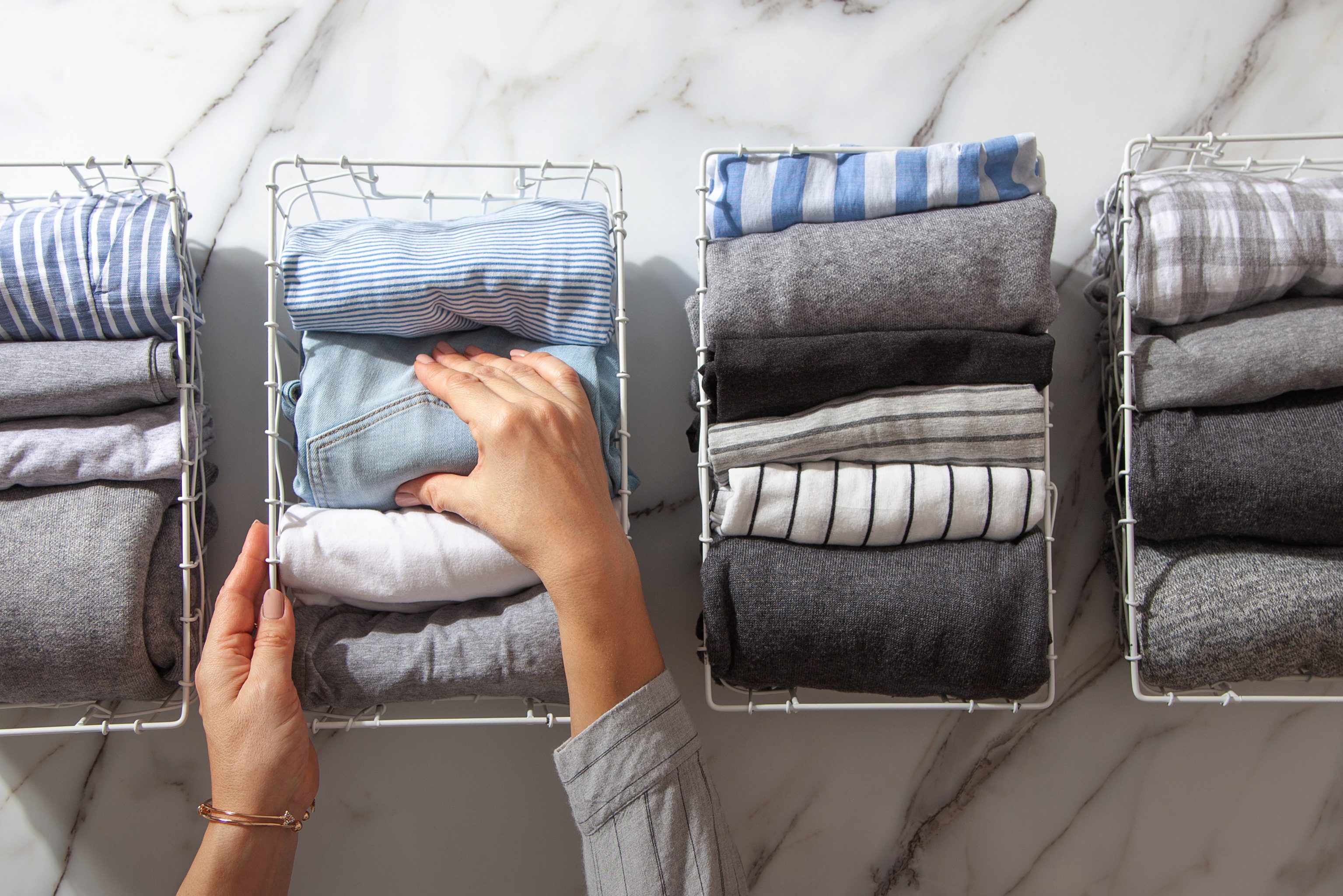 hands organizing folded clothes in wire baskets