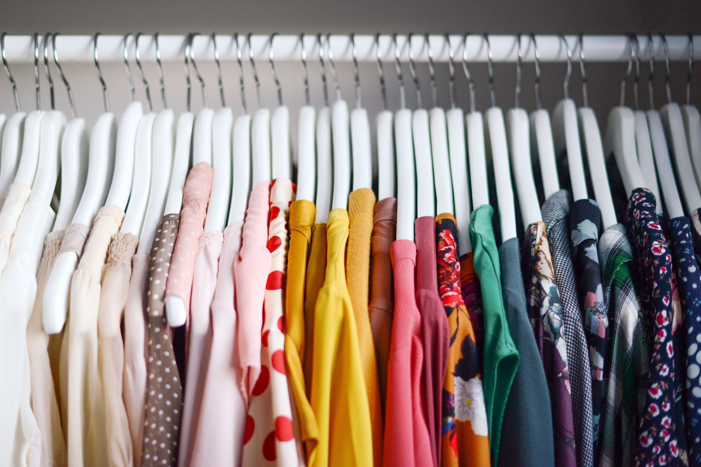 clothes hanging on white wood hangers organized by color, light to dark, on a rod in a closet