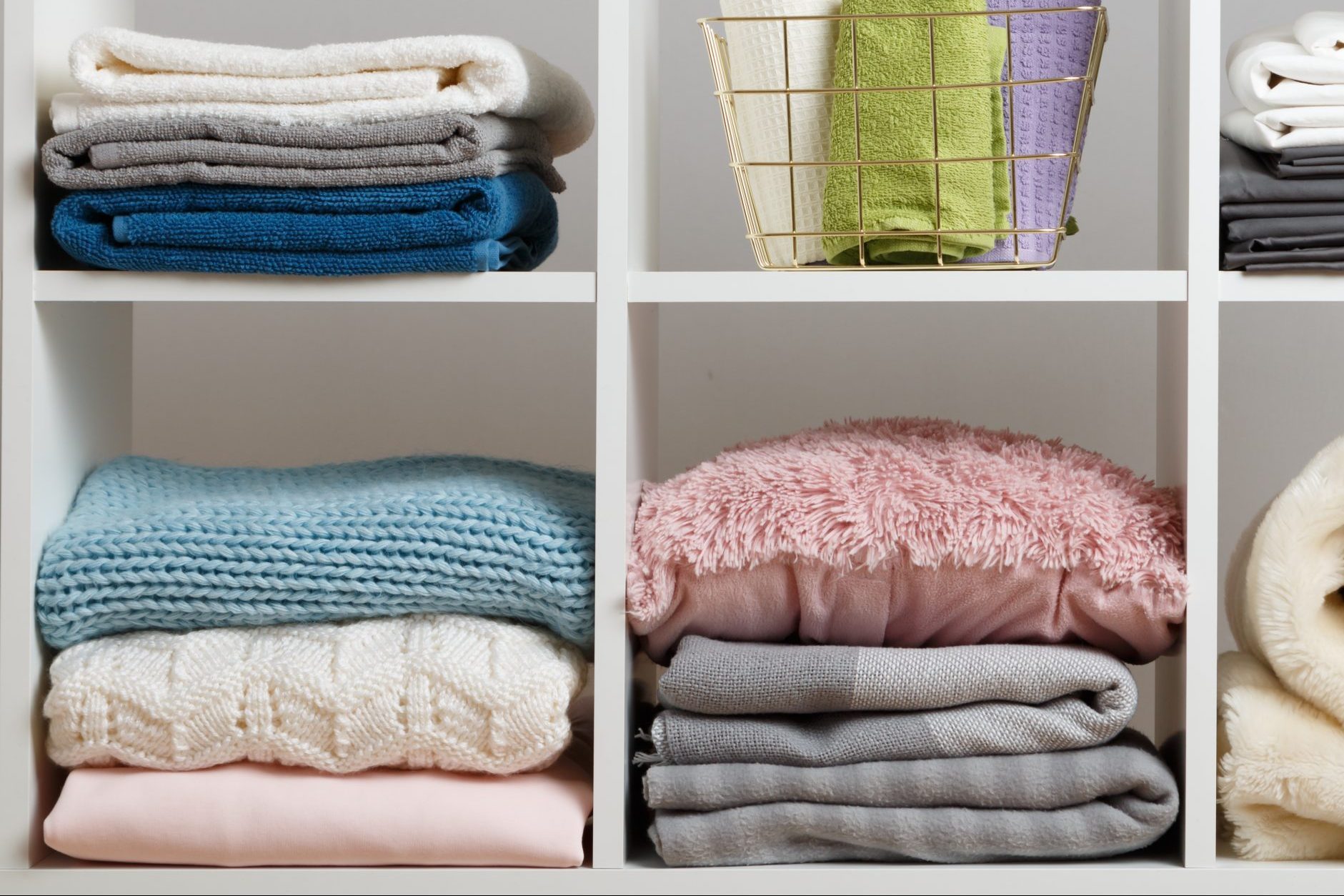 Stacks of towels, sheets, bedding, clothes, blanket and pillow on a white shelf.