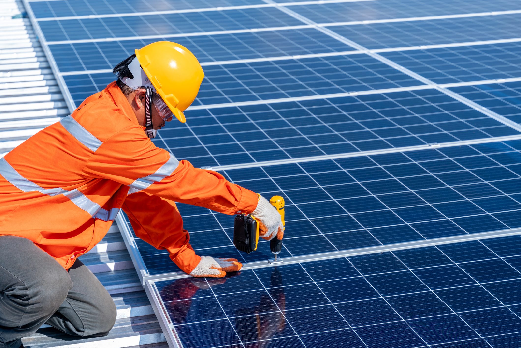 Asian technicians using an electric drill installing solar cells to produce and distribute electricity. Solar energy technology concept