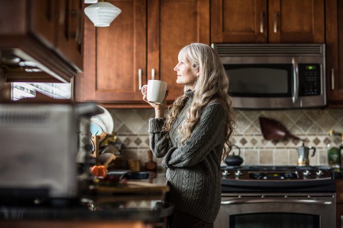 Portrait of woman (60yrs) having coffee in kitchen