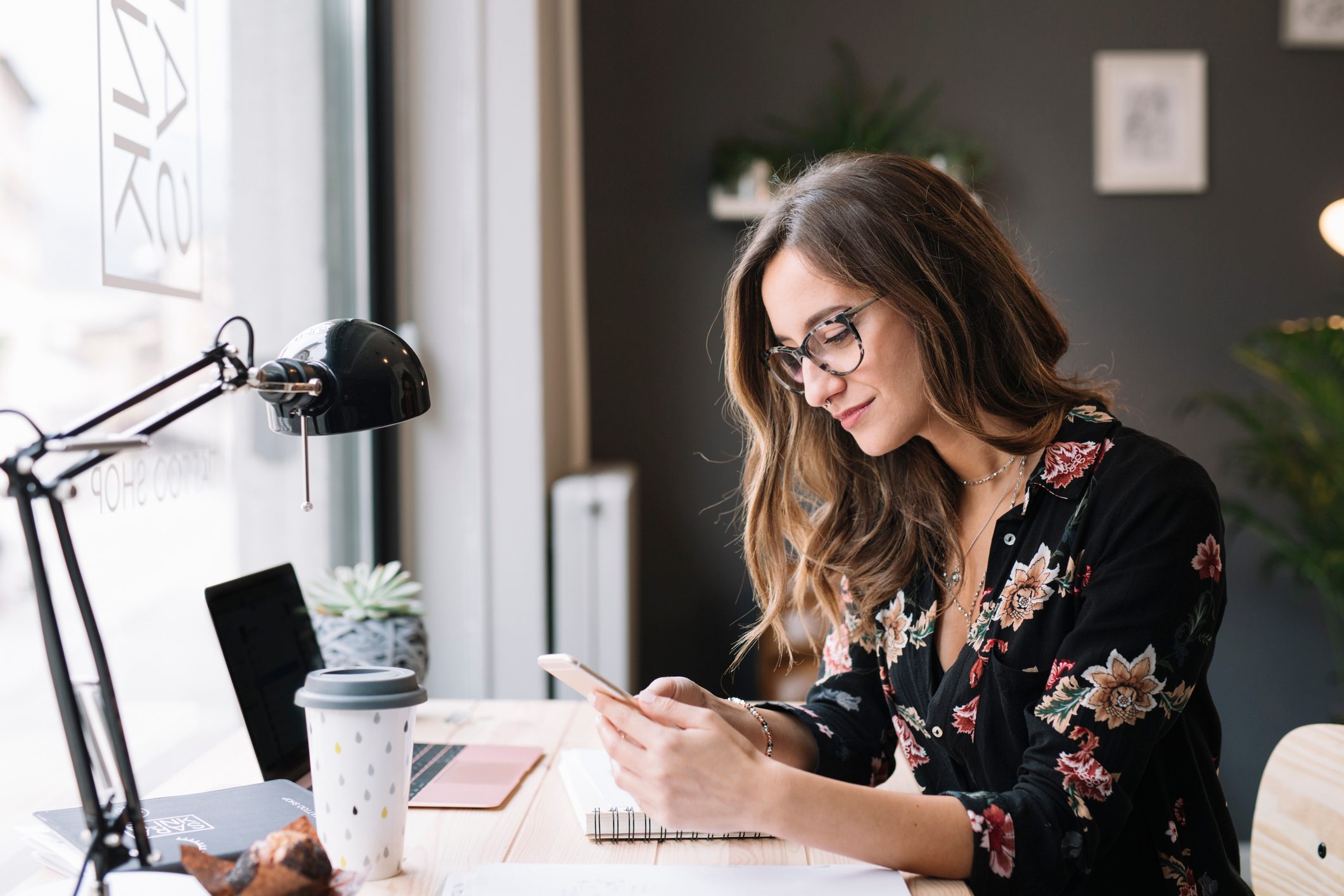 Smiling woman sitting at desk in tattoo studio looking at cell phone