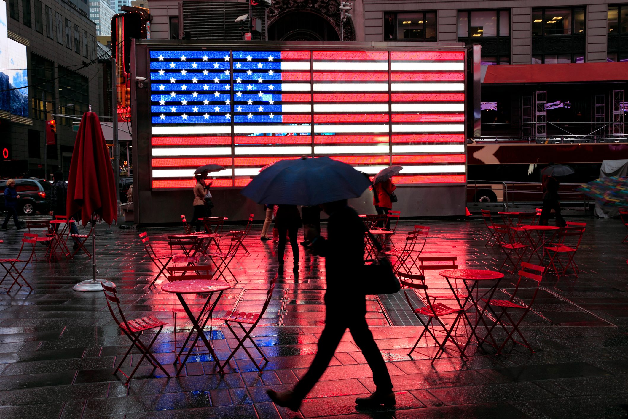 City in the Rain: silhouette of pedestrian with umbrella passing famous LED american flag in wet Times Square