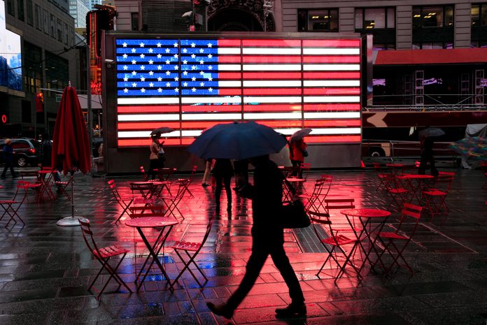 City in the Rain: silhouette of pedestrian with umbrella passing famous LED american flag in wet Times Square