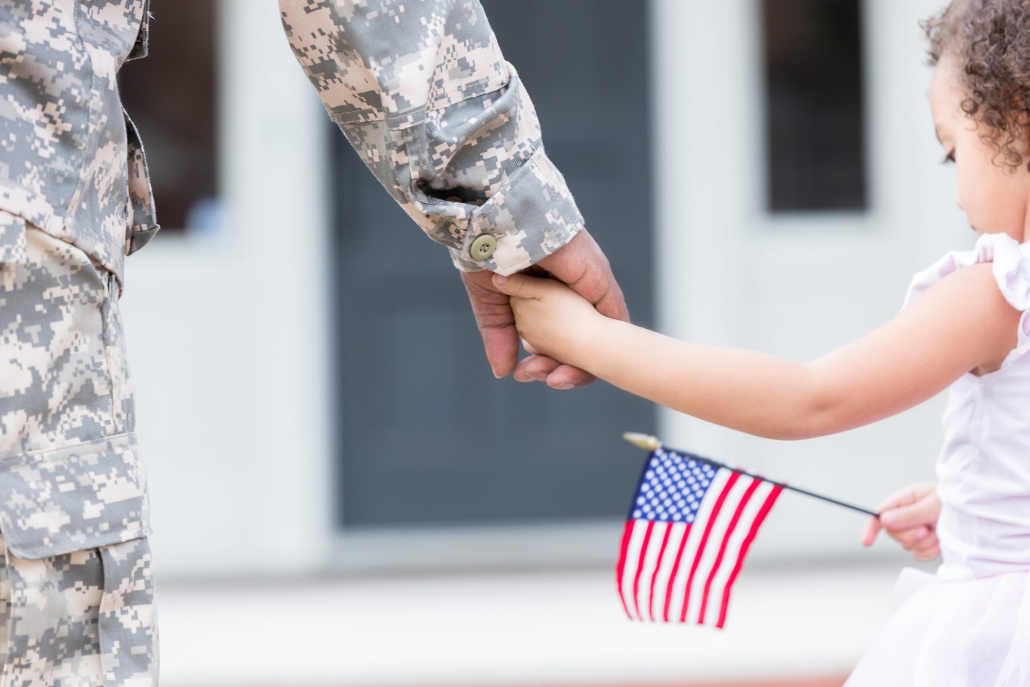 Soldier and his young daughter walk hand in hand and the daughter holds a small american flag