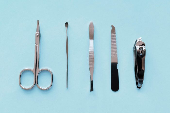 Travel-size manicure tools (scissors, cuticle pusher, tweezers, nail file and nail clippers) on soft blue background